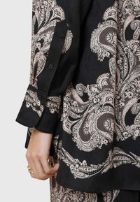 Camicia di stoffa nera con motivo paisley rosa, caratterizzata da maniche lunghe con risvolto e dettaglio di bottone sulla manica. Texture liscia.