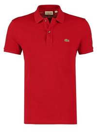 Red polo shirt made of textured cotton, featuring a classic collar, two-button placket, and a green embroidered crocodile logo on the chest.