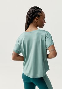 Mentolovo zelené tričko s krátkym rukávom, vo voľnom strihu a s prehnutými rukávmi, v kombinácii s tyrkysovými legínami. Hladká tkanina a poškodené okraje.