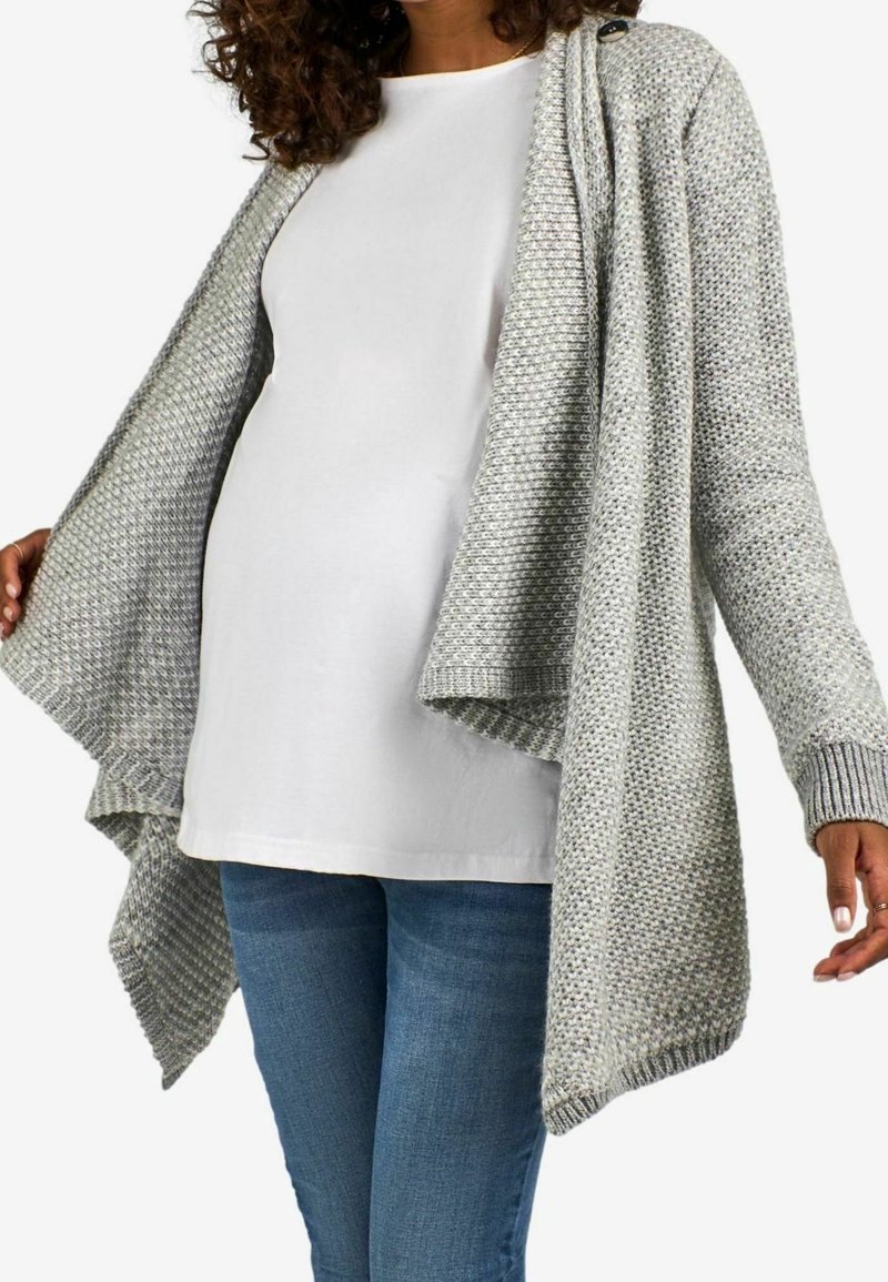 Cardigan gris en maille avec un devant ouvert, un motif texturé et des manches longues. Porté sur un haut blanc et un jean bleu, mettant en valeur une coupe décontractée et un tombé fluide.