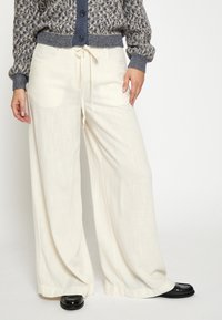 Široke, kremaste hlače iz lahkega materiala z vrvico v pasu. Imajo sprednje žepke in gladko teksturo.