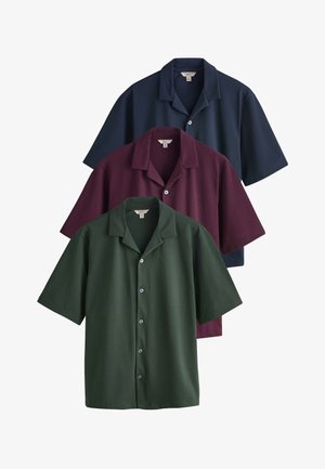 Trzy koszule na krótki rękaw z kołnierzami camp w kolorach granatowym, bordowym i ciemnozielonym, ułożone pionowo na białym tle.