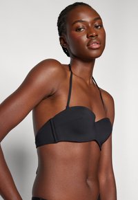 Haut bandeau noir avec un design incurvé, texture lisse et bretelles ajustables. Présente une zone de soutien-gorge structurée et un style minimaliste.