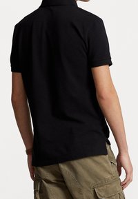 Svart polo t-shirt med korta ärmar, kragdesign och texturerad tyg. Bärs med ljusa khaki cargo-shorts, visar bakvyn.