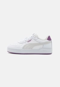 Sneaker bianca con tomaia in pelle testurizzata, dettagli viola e punta perforata. Presenta una suola bianca spessa e una distintiva striscia laterale.