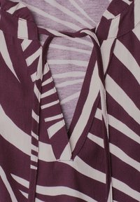 Gros plan d’un tissu rayé violet et blanc avec un col en V et un détail de lien en tissu.
