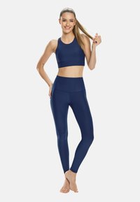 Sostenedor deportivo azul marino y leggings de cintura alta fabricados con un tejido suave. Ambos presentan un diseño simple sin patrones visibles ni herrajes.