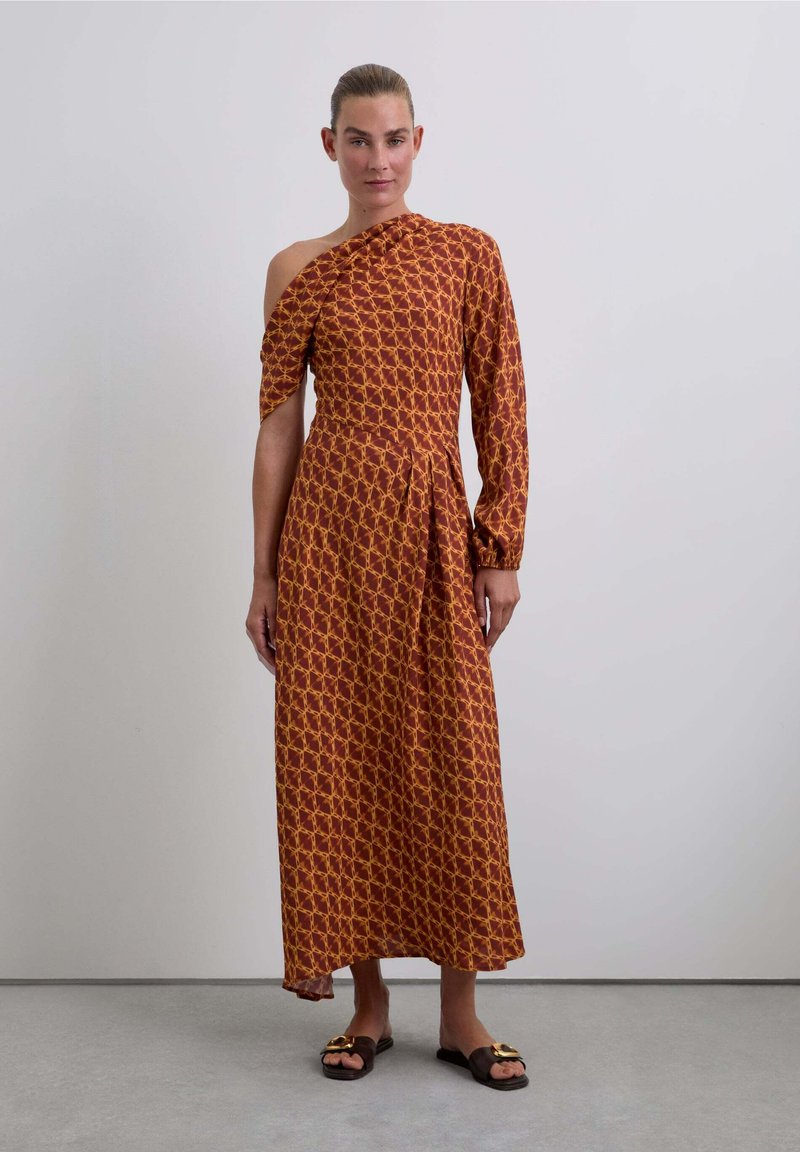 Maxi jurk van bruine stof met een geel geometrisch patroon, een schouderontwerp, lange mouwen en een ingebouwde taille, gecombineerd met bruine slip-on sandalen.