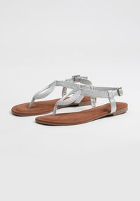Sandalias planas plateadas con un diseño de tira texturizada, plantilla de ante sintético marrón y una hebilla ajustable en el tobillo para un mejor ajuste.