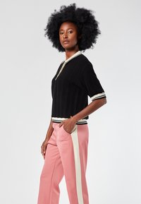 Top negro de manga corta con textura acanalada, cuello blanco y dobladillo a rayas, combinado con pantalones rosas que incluyen un panel lateral blanco y bolsillos.