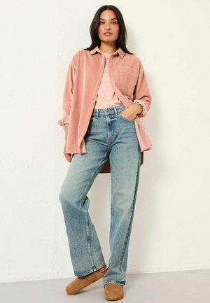 Light pink corduroy shirt over a light top, paired with faded blue wide-leg jeans and brown suede slip-on shoes. Simple, casual design.