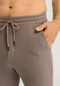 Lichtbruine, zachte joggers van stof met een elastische tailleband, een koordsluiting en zijzakken. Geweven oppervlak met een subtiel patroon.