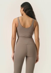 Bruine aansluitende tanktop en bijpassende leggings van rekbaar materiaal. De tanktop heeft een ronde rug en de leggings hebben een hoge tailleband.