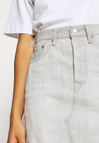 Jupe en denim gris avec taille haute, poches avant et accents de quincaillerie ton cuivre. Texture lisse avec détails cousus.