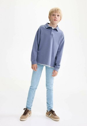 Ljusblå bomullspolo med lång ärm, matchad med blekta blå skinny jeans och bruna sneakers med vita detaljer.