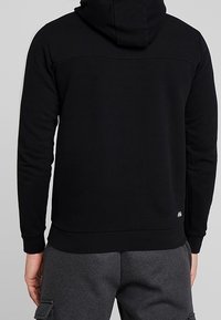 Sudadera negra con una silueta ajustada, puños y dobladillo acanalados. Cuenta con un bolsillo tipo canguro y un sutil detalle de logo en la parte inferior.