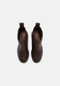 Bottines en cuir marron avec panneaux élastiques sur les côtés et languettes, présentant une texture lisse et un design à bout rond.