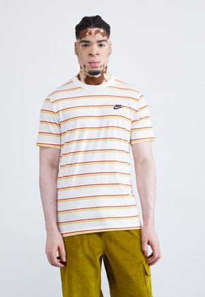 Camiseta blanca a rayas con líneas horizontales rojas y amarillas, cuello redondo y un logo negro de Nike en el lado izquierdo del pecho.