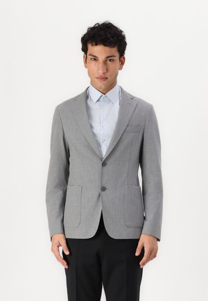 Blazer grigio chiaro con rever a punta, due bottoni e due tasche frontali. Indossato sopra una camicia a righe blu e bianca. Texture liscia.