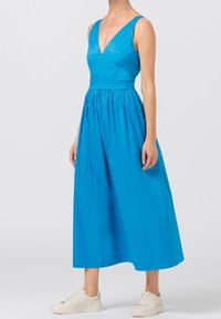 Blå ärmlös klänning med djup V-ringning, cinchad midja och full kjol. Smooth tyg med en solid färg, bärs med vita sneakers.