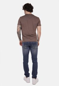 Camicetta marrone a maniche corte, jeans blu, sneakers. La camicetta ha una finitura testurizzata; i jeans presentano una vestibilità classica con tasche posteriori.