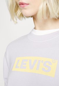 Jasnoszara bluza z bawełny, z wyrazistym żółtym logo "LEVI'S" z przodu. Okrągły dekolt o gładkiej fakturze.
