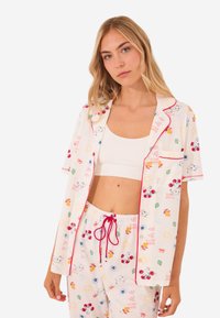 Lyhythihainen pyjamapaketti valkoisesta puuvillasta, jossa on värikkäitä hedelmä- ja auringon kuvioita. Sisältää punaisia teippejä ja kiristettävän vyötärön.