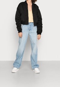 Svart bomberjacka med ribbade ärmslut, kombinerad med ljusblå vida jeans och vita sneakers. Jackan har dragkedjestängning och sidofickor.