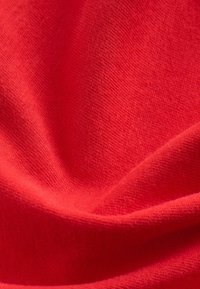 Tessuto di cotone rosso con una consistenza morbida, caratterizzato da una trama liscia e uniforme. Il materiale si drappeggia in modo fluido, creando pieghe delicate.