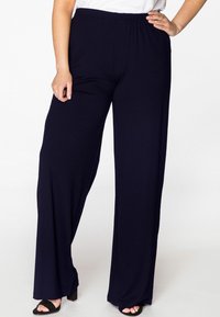 Maritieme wijde broek met een elastische tailleband, gemaakt van zachte stof. Kenmerkt zich door een gladde textuur en een losse pasvorm, gedragen met zwarte haksandalen.
