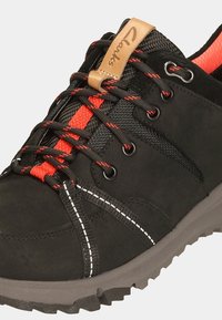 Black footwear with textured upper, red and black laces, and a tan leather tag. Features a rugged grey sole and white stitching accents.