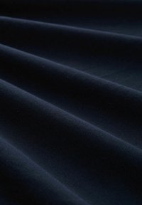 Tmavě modrá látka s diagonálním jemným žebrovaným vzorem, s hladkými sklady a subtilním leskem. Zobrazený materiál vypadá pevně a tkaně.