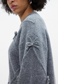 Pilkos megztos su akcentais ant rankovių, tekstūruoto audinio ir laisvo kirpimo. Dizainas pabrėžia delikačią, švelnią išvaizdą.