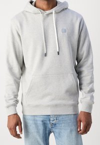 Sudadera con capucha gris, con un bolsillo tipo canguro, cuerdas blancas y un pequeño parche cuadrado en el pecho. Tejido suave con puños acanalados.