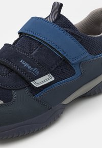 Niebieskie dziecięce sneakersy z rzepem, wykonane z siateczki i zamszu. Posiadają teksturowaną podeszwę oraz szare akcenty dla lepszego wsparcia.