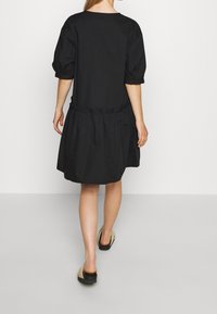 Černé bavlněné šaty s balónovými rukávy, kulatým výstřihem a nařaseným pasem. Sukně je rozevlátá a sahá do poloviny stehna. Nošeny s béžovými sandály.