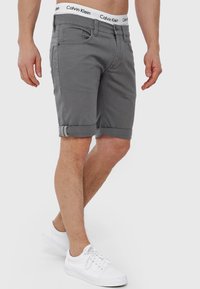 Grå denim shorts med omslået kant, med forlommer og en hvid Calvin Klein talje. Bæres med hvide sneakers.