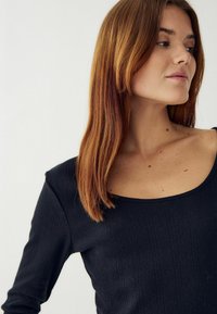 Čierny dlhý rukáv top s okrúhlym výstrihom, so žebrovanou textúrou a vertikálnymi pruhmi. Materiál vyzerá mäkký a pružný.