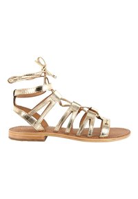 Sandalia plana de tiras metálicas doradas, con diseño de punta abierta, lazos en el tobillo y tacón estilo madera. Presenta múltiples tiras delgadas.