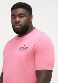 Pink short-sleeve t-shirt in cotton blend with crew neck, featuring a printed logo "HILFIGER NEW YORK 1985" on the chest. Smooth texture.