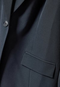 Ciemnoniebieska marynarka z teksturowanej tkaniny, zapinana na pojedynczy guzik, z kieszonką naszytą po lewej stronie. Gładkie wykończenie i dopasowany krój.