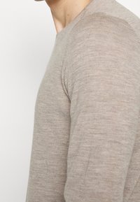 Hellbeiger, langärmliger Strickpullover mit glatter, feiner Struktur und angesetztem Schnitt sowie rundem Ausschnitt und nahtlosen Schultern.