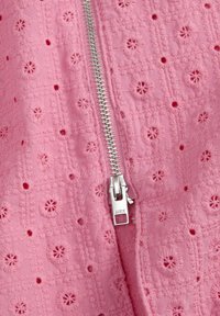 Ružičasta pamučna tkanina s izveznim cvjetnim uzorcima, s metalnim zatvaračem u srebrnoj boji sprijeda. Tekstura izgleda izbočena i detaljna.