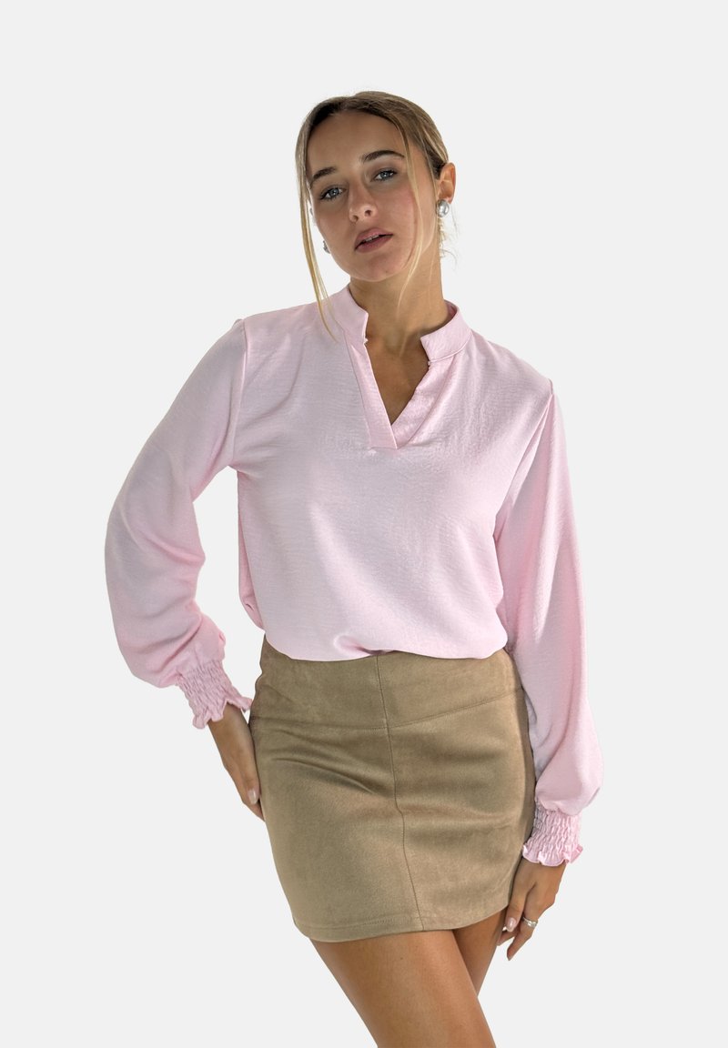 Lichtroze blouse met lange mouwen, een kraag en gegatherde manchetten, gecombineerd met een tan kleurige suède mini rok. Gladde textuur.