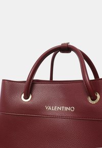 Sac fourre-tout en cuir bordeaux avec quincaillerie dorée, doté de poignées doubles arrondies et d'un logo "VALENTINO" en relief à l'avant. Fini texturé.