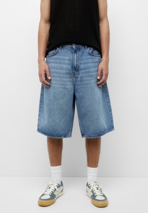 Denim shorts in light blue, featuring a loose fit and knee-length design. Worn with a black sleeveless top and sneakers.