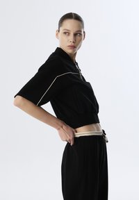 Black cropped jacket with short sleeves, featuring a zipper and light beige accent stitching. Paired with black high-waisted pants.