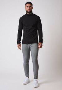 Sort langærmet turtleneck trøje parret med grå tætsiddende bukser og hvide sneakers. Glat stof, minimal logoer og slankt design.