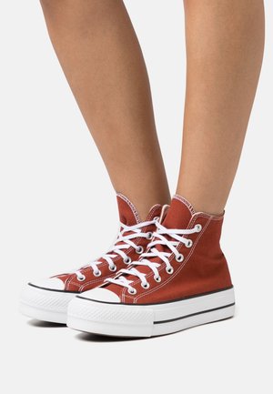 Hoge sneakers in roestkleurige canvas met witte oogjes en veters, zwarte streep op de middenzool en rubberen neuskap.