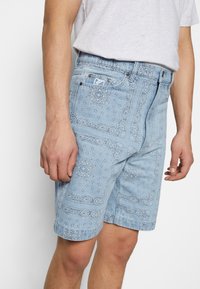 Lichtblauwe denim shorts met een bandana patroon, vijf zakken en metalen hardware. De stof heeft een zachte, gestructureerde afwerking.